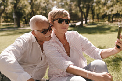 blonde-lady-sunglasses-striped-stylish-blouse-jeans-sitting-grass-making-selfie-with-mustachioed-man-white-shirt-outdoor.jpg
